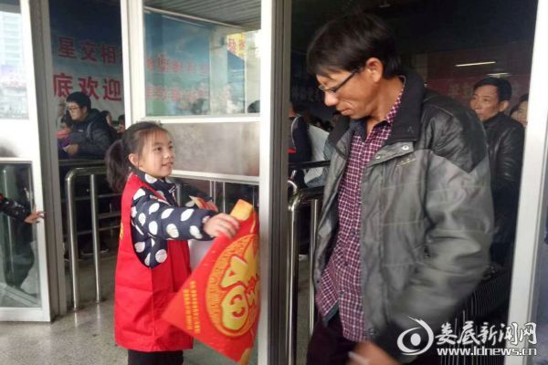 （9岁的杨景琪边和志愿者们一起在火车站志愿服务站点，为有需要的旅客送福字、送对联和《便民服务手册》）