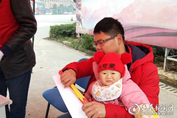 （志愿者彭军飞抱着自己9个月大的女儿来参加2019·温暖回家路志愿服务）