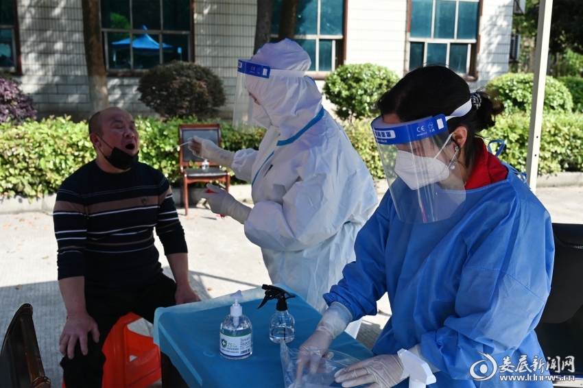 （娄星产业开发区企业服务中心负责人彭雄辉正穿着简易防护服协助医生做检测前信息核对工作。她是这是她坚持战斗在核酸检测点的第3天。）